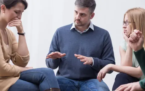 Uomo con aria autoritaria parla a un gruppo, una donna piange. Sembra un collega che vuole comandare.