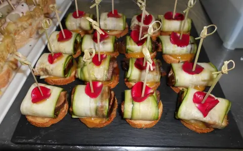 Variedad de tipos de pinchos con calabacín enrollado, pétalos rojos y palillos de bambú.