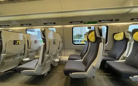 Wnętrze pociągu Pendolino z rzędami szarych foteli z żółtymi zagłówkami.