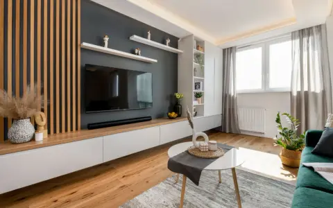Nowoczesny salon z lamelami inspiracje: drewniane panele, szara ściana z TV, białe meble i zielona kanapa tworzą przytulną przestrzeń.
