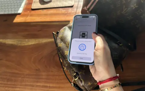 Dłoń trzymająca telefon z aplikacją NFC nad torebką Louis Vuitton.