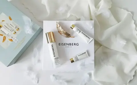 Luksusowe kosmetyki EISENBERG w eleganckim zestawie, otulone delikatnymi piórkami i złotym liściem.