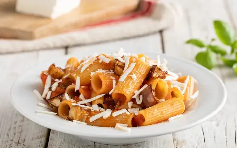 Piatto di pasta alla norma con rigatoni, melanzane fritte, pomodoro e ricotta salata grattugiata.
