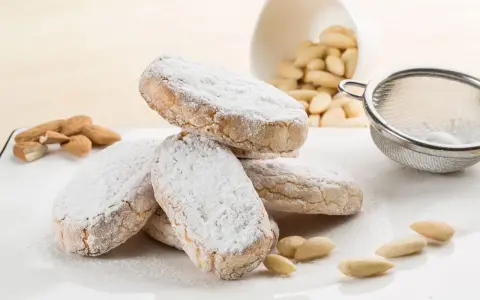Dolce di Siena cosparso di zucchero a velo, con mandorle e setaccio sullo sfondo.