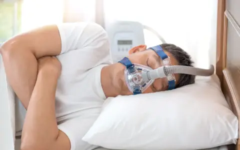 Mężczyzna śpi z maską CPAP, która pomaga mu oddychać podczas snu, łagodząc objawy bezdechu nocnego.