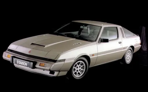 Klasyczny Mitsubishi Starion w kolorze szampańskim, z charakterystycznym wlotem powietrza na masce i sportowym nadwoziem coupe.