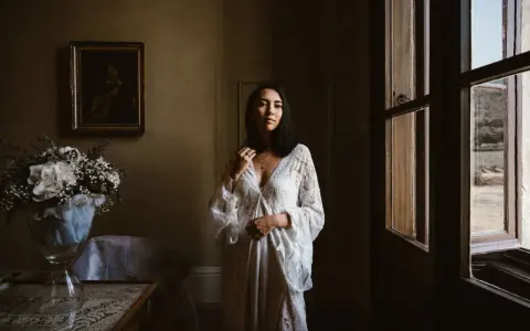 Kobieta w białej sukni, obok bukiet kwiatów. Scena sugeruje przygotowania do ślubu za granicą, co wyjaśnia przyczyny popularności wesel typu "destination wedding".