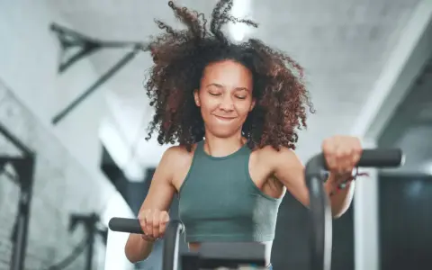 Frau mit lockigem Haar trainiert intensiv auf einem Fahrrad. Sie gibt alles, was ist HIIT – High Intensity Interval Training.