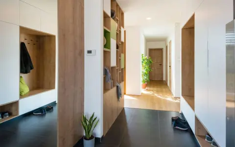 Ingresso moderno con armadi bianchi e legno, mensole a giorno per arredare ingresso, scarpe e piante.