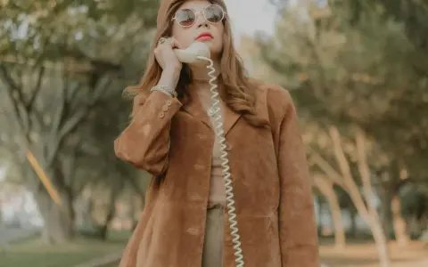 Kobieta w brązowej zamszowej kurtce damskiej rozmawia przez telefon w stylu retro.