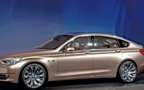Eleganckie, złote bmw gt z przyciemnianymi szybami i chromowanymi felgami stoi na tle niebieskiej ściany.