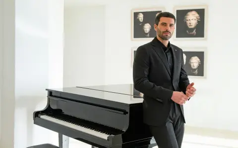 Uomo con elegante outfit per andare a teatro, in completo nero, accanto a un pianoforte a coda.
