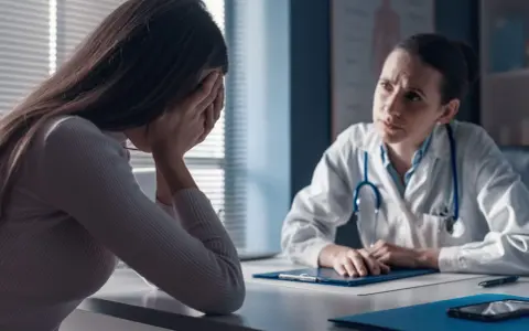 Kobieta w gabinecie lekarskim, ze smutkiem ukrytym w dłoniach, słucha diagnozy. Lekarka z troską pochyla się nad dokumentami, być może omawiając poronienie chybione.