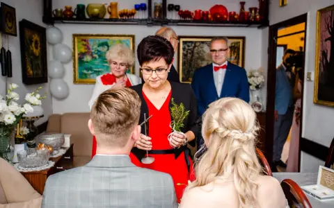 Rodzina udziela błogosławieństwa młodej parze. Kobieta trzyma gałązkę ziół, symbolizującą pomyślność.