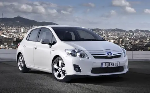 Biała Toyota Auris hybryda na tle miasta. Czy warto zainwestować w ten model?