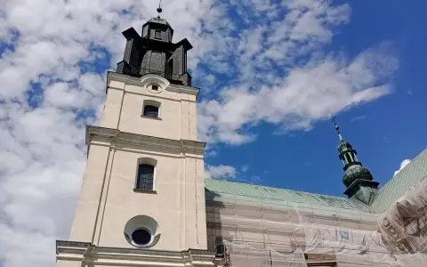 Wieża kościoła w Gidlach pod błękitnym niebem z chmurami. Widać fragment dachu w rusztowaniach.