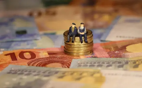 Dos figuritas sentadas en monedas de oro sobre billetes de euros. Reflexionan: como puedo cotizar los años que me faltan.