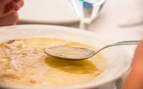 Caldo de pollo casero en un plato blanco con una cuchara.