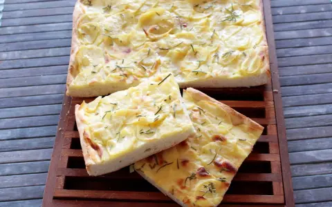 Focaccia con lievito istantaneo, ricca di patate e rosmarino, servita su un tagliere di legno.