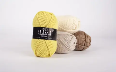 Gula, beige, ljusbruna och vita nystan av Drops Alaska garn ligger i en hög.