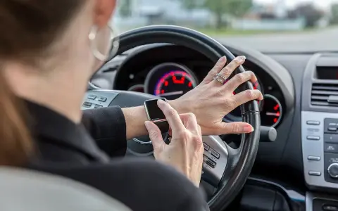 Frau tippt auf ihre Smartwatch am Steuer. Handy am Steuer Strafe vermeiden!