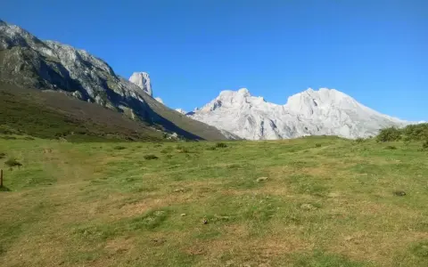 Majestatyczne szczyty Picos de Europa, w tym charakterystyczny Torre de Cerredo, wznoszą się nad zieloną doliną.