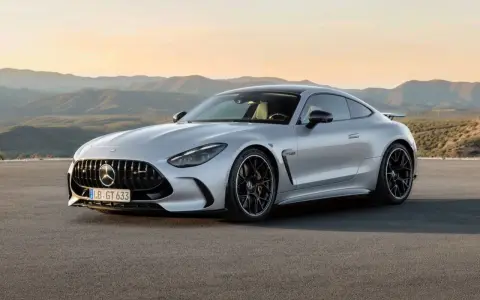 Un elegante Mercedes GTR plateado descansa en una carretera desierta, con montañas onduladas al atardecer de fondo.