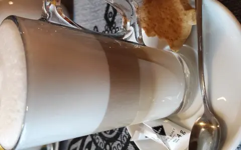 Kawa latte w szklance, obok ciasteczko i cukier. Idealna na przerwę w karczmie u wróbla menu.