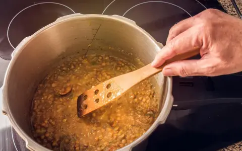 Lentejas deliciosas cocinándose en olla express, removidas con cuchara de madera.