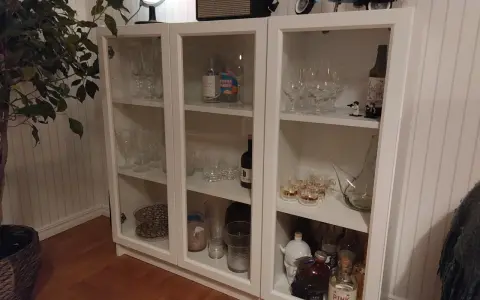 Ett DIY-projekt med ett vitt Billy vitrinskåp fyllt med glas, flaskor och dekorationer.
