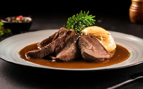 Zartes Tafelspitz-Rezept auf einem Teller mit Sauce, Beilage und Rosmarinzweig.