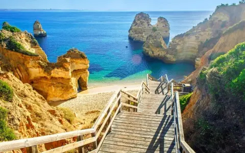 Schody prowadzą na piaszczystą plażę z turkusową wodą i skalnymi formacjami. To idealne miejsce, by zobaczyć, co Portugalia ma do zaoferowania.