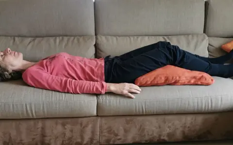 Donna sdraiata sul divano con un cuscino sotto le ginocchia per una postura corretta seduti divano.