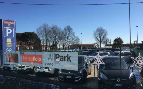 Parcheggio vicino all'aeroporto di Venezia Treviso con cartelli Marco Polo e All Park. Auto parcheggiate sotto un cielo azzurro.