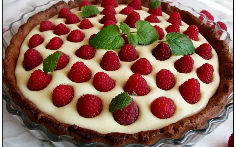Tarta z mascarpone i białą czekoladą, ozdobiona malinami i miętą. Pyszny deser na każdą okazję.