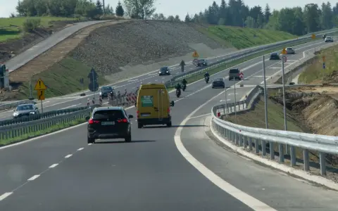 Droga ekspresowa z samochodami i motocyklami, gdzie panuje bezpieczna prędkość. W tle widać prace budowlane.