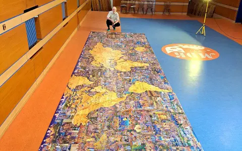 Mężczyzna kuca przy największych puzzlach na świecie, przedstawiających mapę świata z detalami miast.