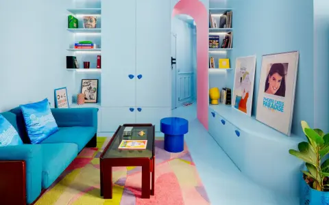 Salón pequeño con sofá azul, alfombra geométrica y estanterías llenas de objetos. Los colores pastel y vibrantes son ideales como colores para pintar salones pequeños.