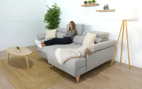Mujer relajada en un sofá en medio del salón, con una manta y cojines.