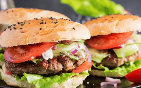 Dwa soczyste burgery wołowe z bułką, pomidorem, sałatą i ogórkiem.