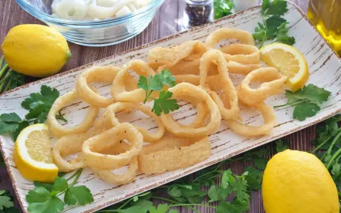 Calamares a la andaluza crujientes y dorados, servidos con limones frescos y perejil.