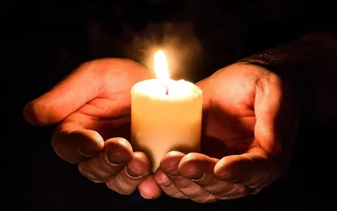 Hände halten eine brennende Kerze, ein Symbol für den Totensonntag, das Licht und Erinnerung spendet.