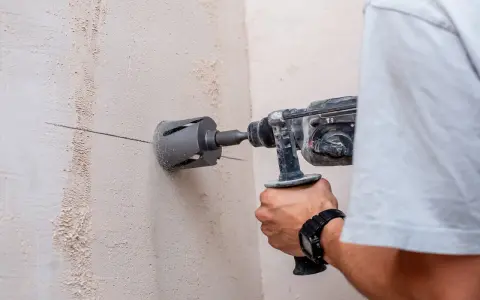 Persona taladra hormigón con una broca de corona. La marca en la pared indica dónde perforar.