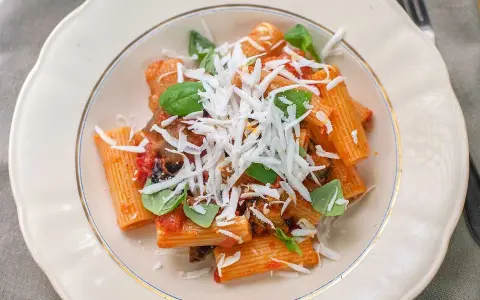 En tallrik med pasta alla norma, toppad med riven ost och färsk basilika.