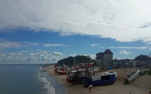 Chłopy trasa: łodzie rybackie na plaży, budynek z czerwonym dachem, morze i niebo z chmurami.