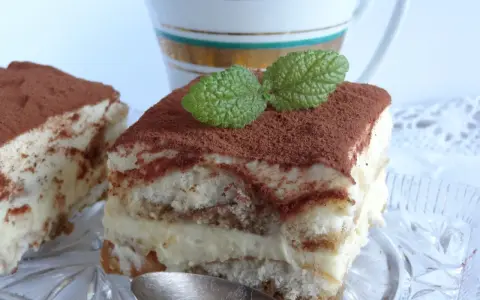 Pyszne tiramisu bezglutenowe, posypane kakao i udekorowane listkiem mięty, czeka na łyżeczkę.