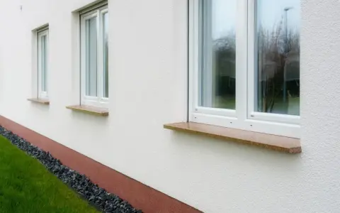 Eleganckie, kamienne parapety przy białym domu. Zastanawiasz się, jak przedłużyć parapet? Ten przykład pokazuje, jak estetycznie można to zrobić.