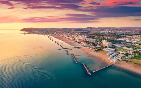 Alba rosa sul cattolica mare, con la costa e le colline sullo sfondo. Una barca solca le acque calme.