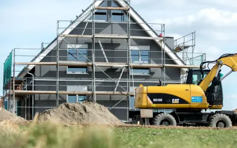 Ein Haus im Bau mit Gerüst und einem Bagger. Die bauseitigen Leistungen sind im vollen Gange.