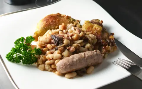 Un plato de el cassoulet con pollo crujiente, salchicha y perejil fresco.
